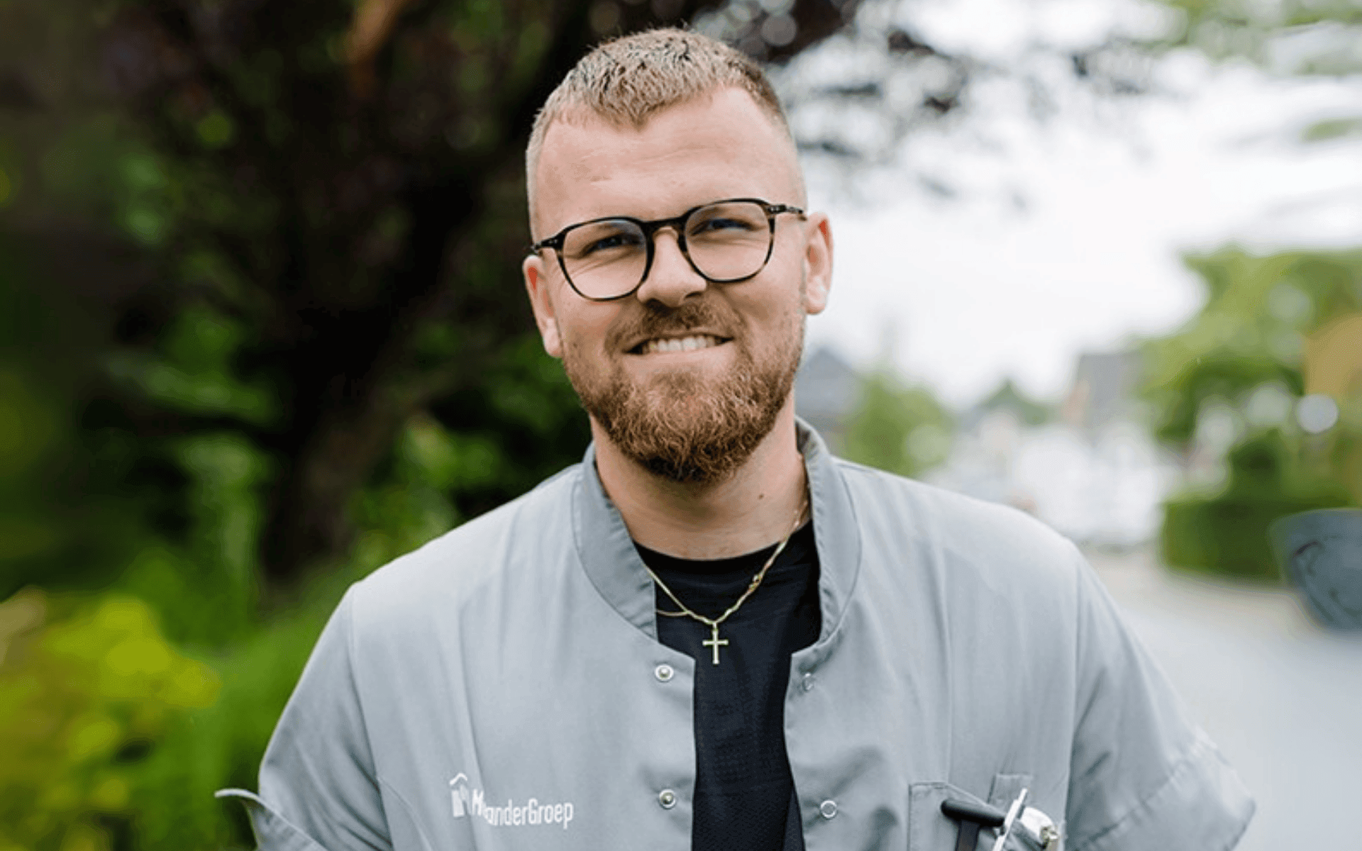 Lachende mannelijke zorgverlener met een bril en een shirt van MeanderGroep.