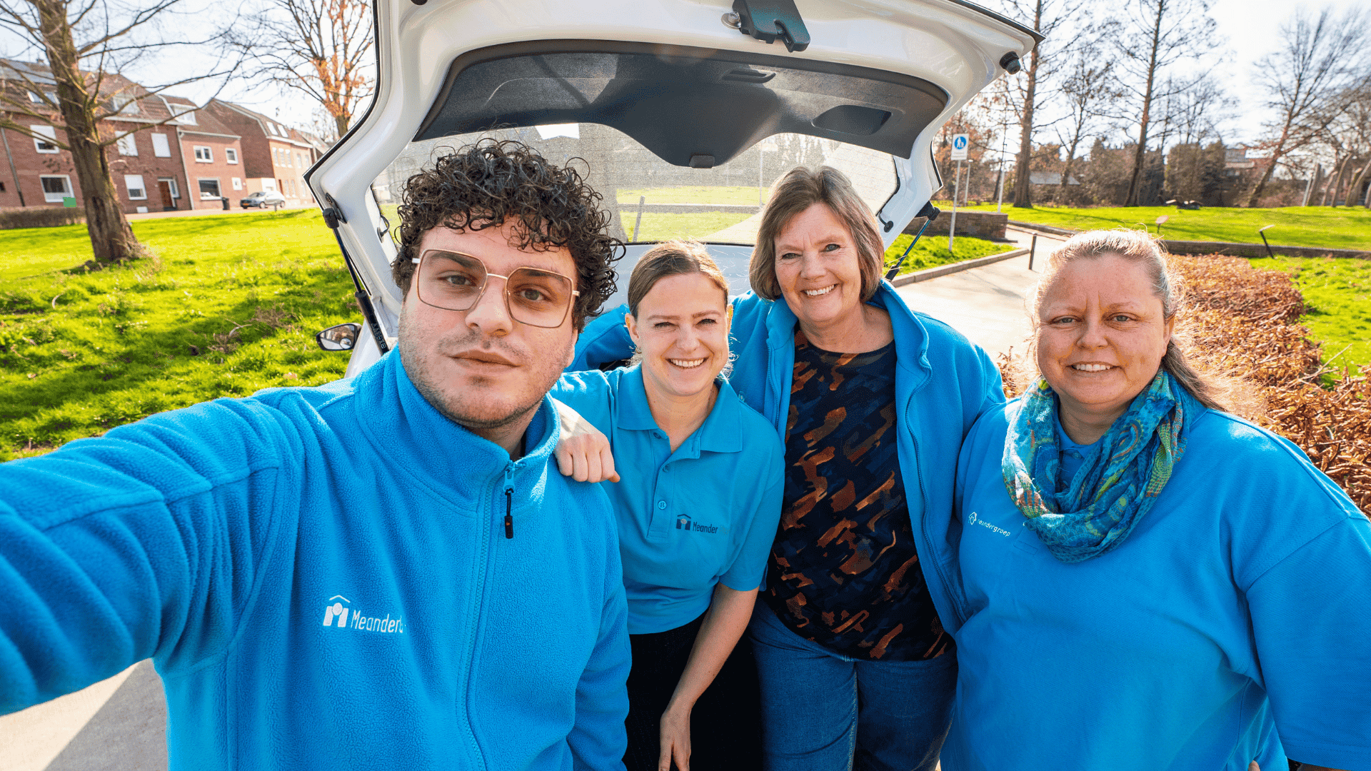 Vier lachende medewerkers maken een selfie in de bedrijfskleding van MeanderGroep.