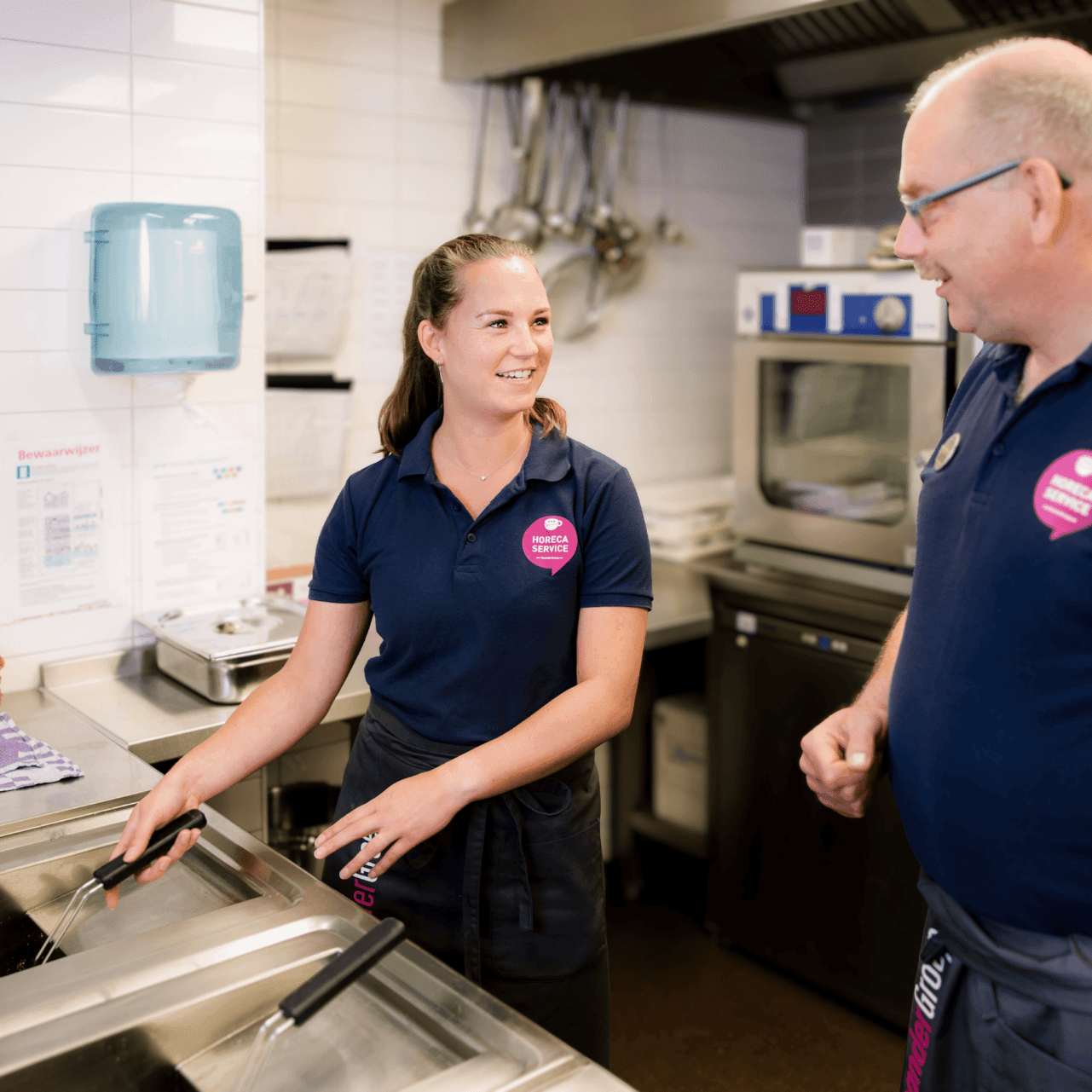 Jonge vrouwelijke medewerker en oudere mannelijke medewerker met donkerblauwe polo's van de horeca service.