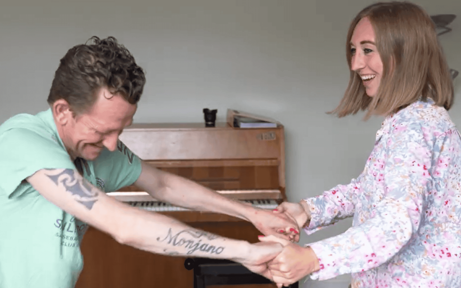 Man met groen shirt danst met vrouw met een blouse met bloemen. In de achtergrond staat een piano.