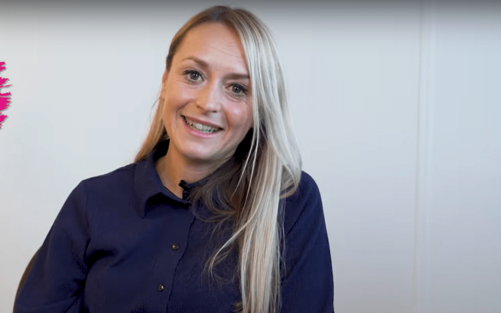 Lachende blonde vrouw met lang blond haar draagt een donkerblauwe blouse. Ze kijkt recht in de camera.